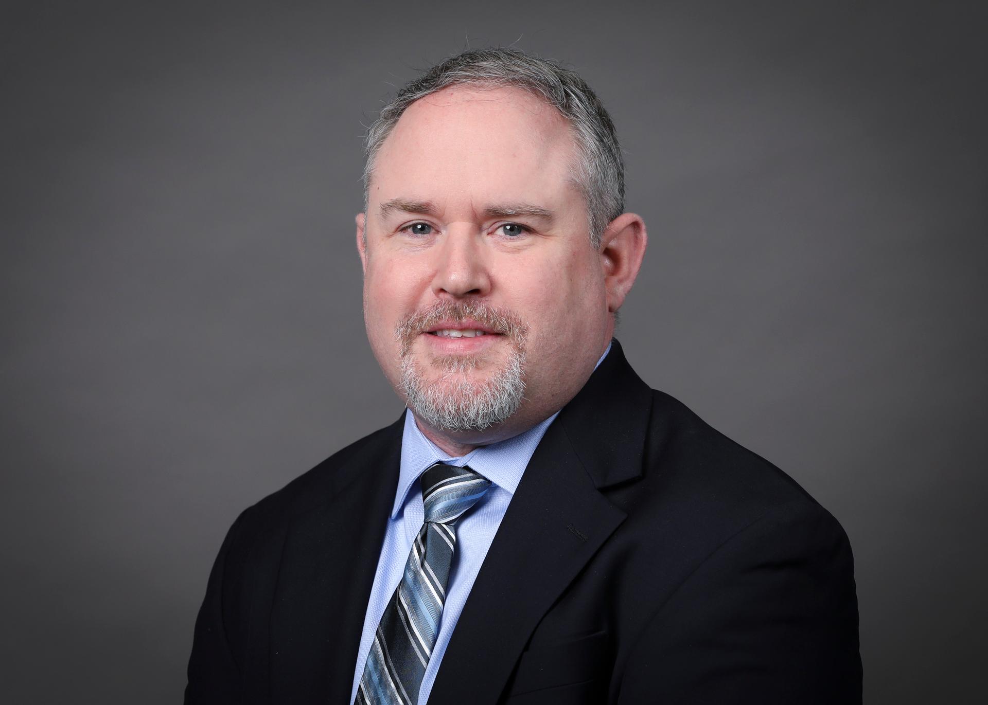 Man in suit and tie in front of grey background.