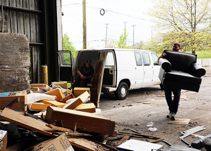 Man carrying chair from truck to trash pile. 
