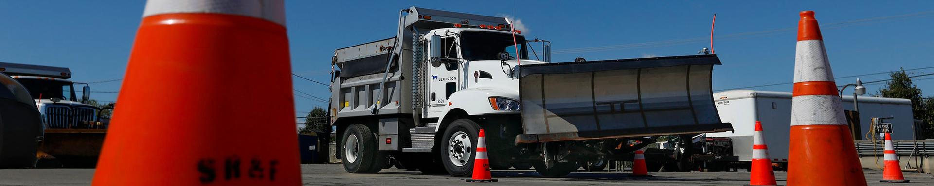 truck with a plow attached driving through orange construction cones